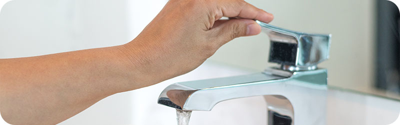 Plan rapproché d'une main ouvrant un robinet pour laisser couler de l'eau